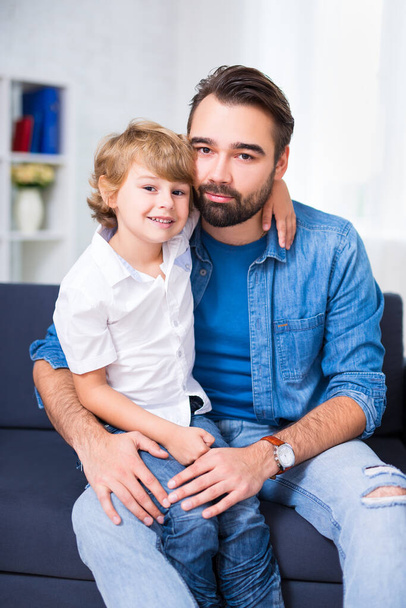 young father and little son sitting on sofa at home - Foto, afbeelding