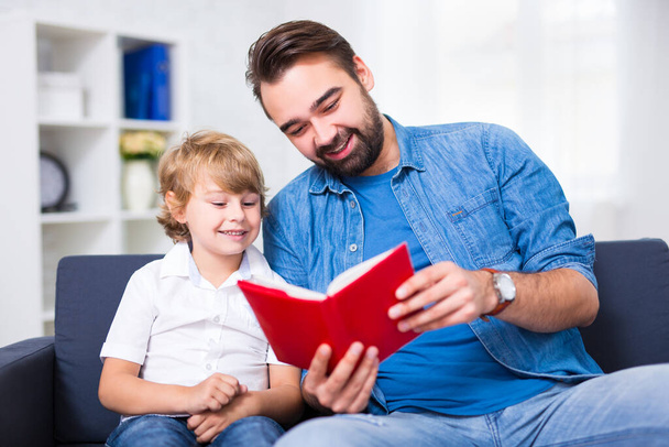 Familien- und Bildungskonzept - Junger Vater liest seinem kleinen Sohn Buch vor - Foto, Bild