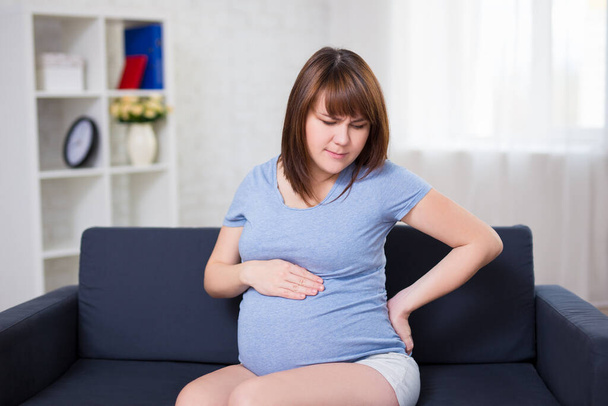 Schwangere leidet unter Bauchschmerzen im Wohnzimmer - Foto, Bild