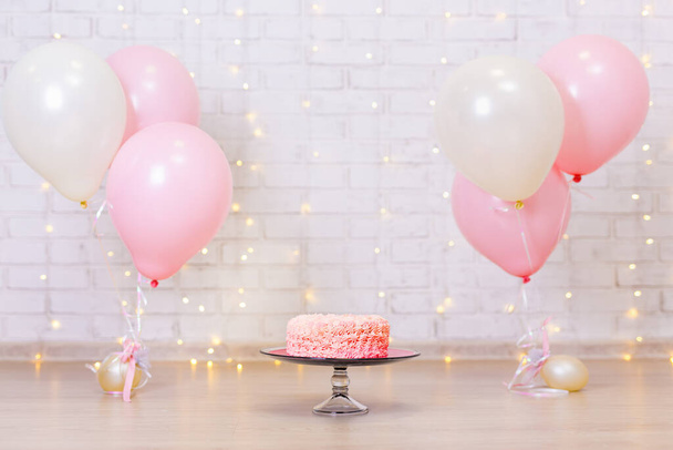 sfondo celebrazione di compleanno - torta alla panna rosa sul muro di mattoni con luci e palloncini - Foto, immagini