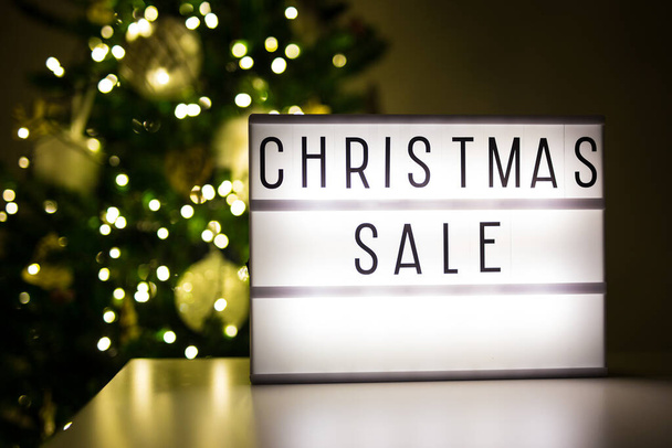 zimní a nákupní koncept - lihtbox s vánočním prodejem text v tmavé místnosti s zdobeným vánoční stromeček - Fotografie, Obrázek