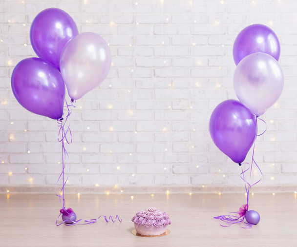 birthday party concept - cake over brick wall background with lights and purple air balloons - Photo, Image