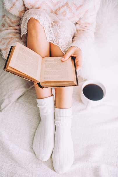 Young woman on the bed with old book and cup of coffee enjoys her stay. - Фото, зображення