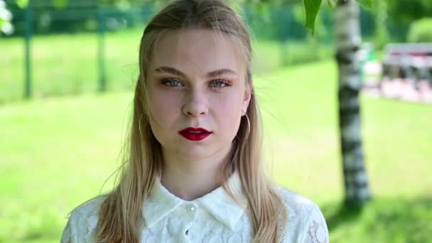 Video van een mooi blond meisje. Portret van een Kaukasisch lachend model met uitstekende make-up in het park bij zonnig weer - Video