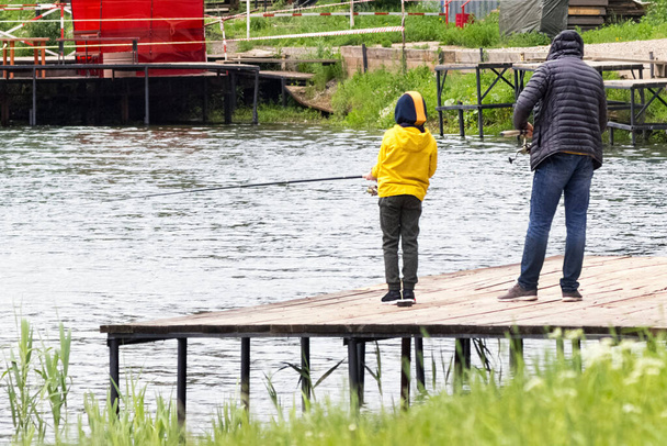 Papà insegna a suo figlio a pescare. concetto di festa del papà. Padre e figlio in giacca gialla pesca insieme - Foto, immagini