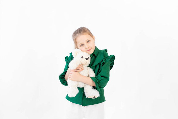 Yeşil elbiseli şirin küçük bir kız oyuncak ayıya sarılıyor, mesaj için yer var, 8 yaşında. - Fotoğraf, Görsel