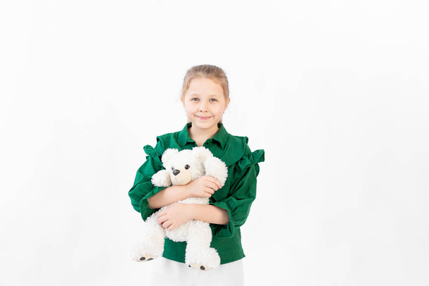 Ein süßes kleines Mädchen in grünen Kleidern umarmt einen Teddybär, Platz für Text, 8-Jährige - Foto, Bild
