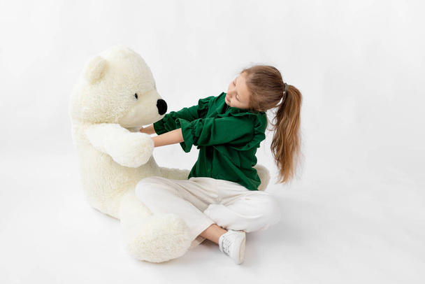 A cute little girl in green clothes hugs a Teddy bear, space for text, 8-year-ol - Foto, afbeelding