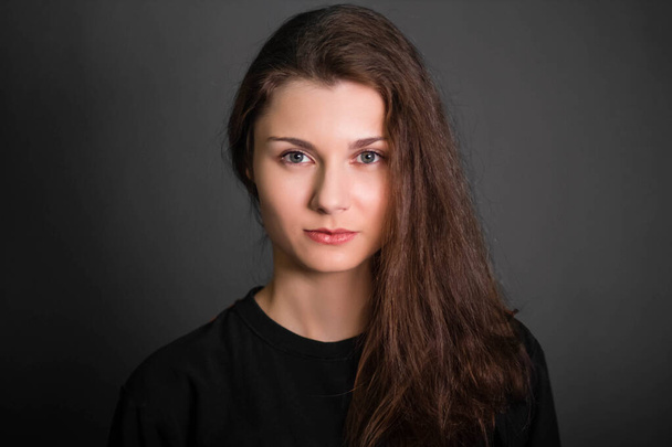 Portrait of a beautiful, young woman in black clothes with long hair. Studio photo, on a gray background. A model with clean skin. - Valokuva, kuva