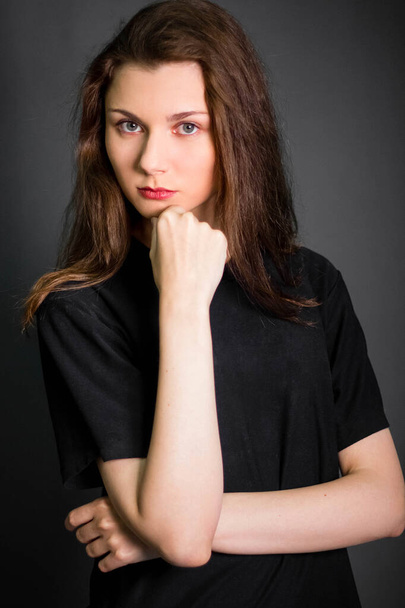 Portrait of a beautiful, young woman in black clothes with long hair. Studio photo, on a gray background. A model with clean skin. - Foto, afbeelding