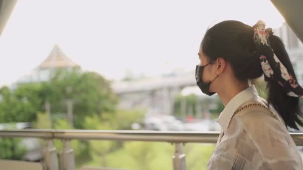 nuori aasialainen nainen käyttää mustaa suojaavaa naamiota seisoo ja katselee aikaa metroasemalla, covid-19 nainen odottaa ystäviä, tapaaminen, itsesuojelu julkisilla liikennevälineillä, kultainen auringonlasku - Materiaali, video
