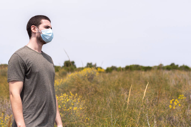 Portrait of a man standing with a face mask in nature with a blue sky on a sunny day looking to the right - Photo, Image