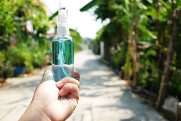 Hand holding a bottle of Ethanol or ethyl alcohol spray for based hand rub is highly effective in reducing influenza a virus on human hands in natural garden. Healthy and Covid-19 epidemic Concept. - Photo, Image