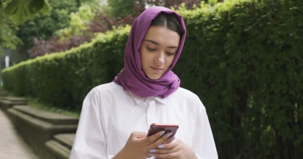 Schöne junge Frau mit traditionellem Kopftuch, die aufs Smartphone schaut. Attraktive Frau im Hidschab - Filmmaterial, Video