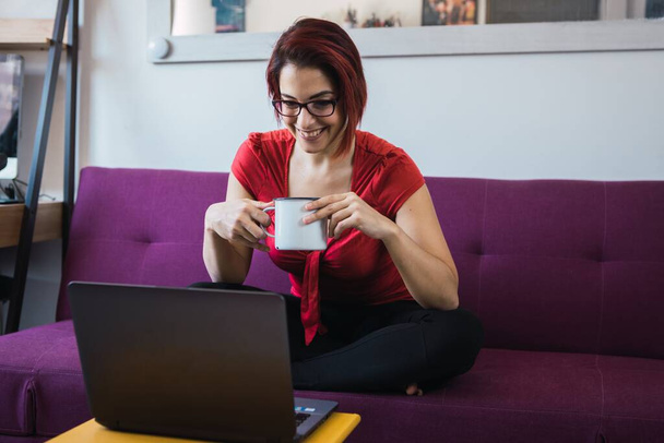 A middle-aged female sitting with a cup in hands and communicating by laptop - Photo, image
