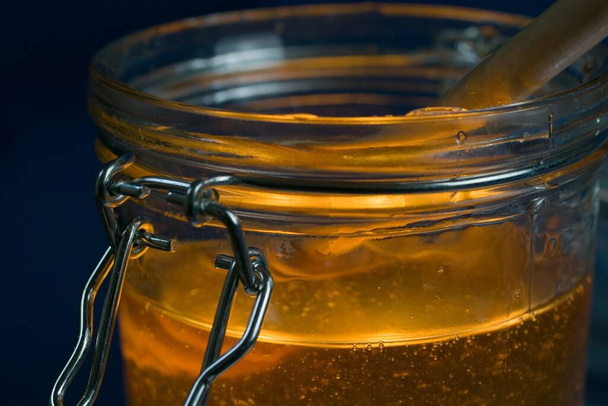 A closeup of a jar of fresh golden honey with wooden honey dipper - Foto, Bild