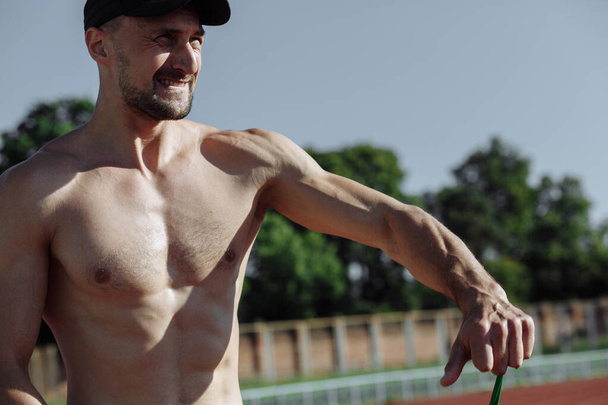 Concentrated shirtless muscular man doing morning workout at the stadium. Sportsman. Strong athletic man - Photo, Image
