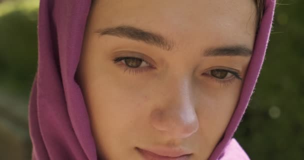 Mooie jonge vrouw die naar de camera kijkt en een traditionele hoofddoek draagt. Aantrekkelijk vrouwtje in hijab. Sluiten. - Video