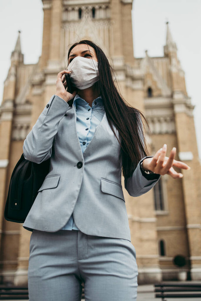 Young and elegant business woman standing on empty city street and wearing protective mask to protect herself from dangerous flu or virus. Corona virus or Covid-19 concept. - Foto, Imagem