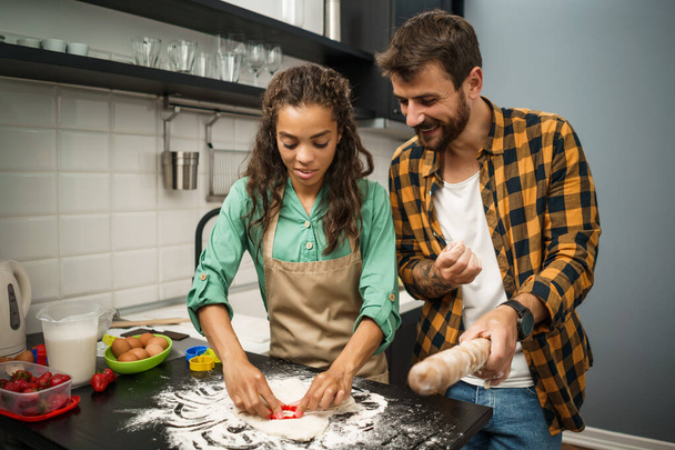 Счастливая многонациональная пара готовит на своей кухне. Они делают печенье
. - Фото, изображение