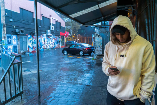 modelo encapuzado em seu telefone justaposicionado para o edifício cheio de carros estacionados em Perth, Austrália Ocidental
 - Foto, Imagem