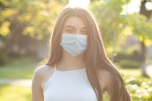 Close up portrait Young woman in medical mask. Female breathes deeply looking at camera. Isolated on park background. Health care and medical concept. - Фото, зображення