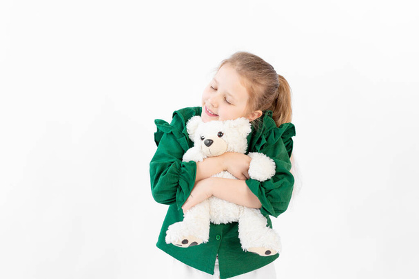 όμορφο κορίτσι σε λευκό φόντο αγκαλιάζει ένα παιχνίδι αρκούδας, 8 ετών, χώρος για κείμενο - Φωτογραφία, εικόνα