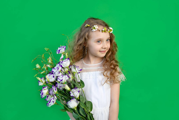 mosolygós 6 éves lány virágokkal, gyönyörű fehér ruhában, zöld háttérrel. szóköz a szövegnek - Fotó, kép