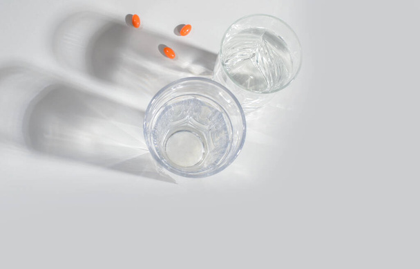 Склянка чистої води з натуральними вітамінами, з тінями на світлому фоні. Вид зверху. охорони здоров'я
 - Фото, зображення