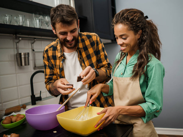 Šťastný multietnický pár vaří ve své kuchyni. Oni dělají sušenky.. - Fotografie, Obrázek