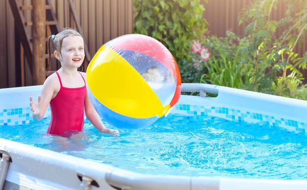 Dívka hraje barevný nafukovací míč v bazénu venkovní, baví. Červené plavky oblečené na dítěti - Fotografie, Obrázek