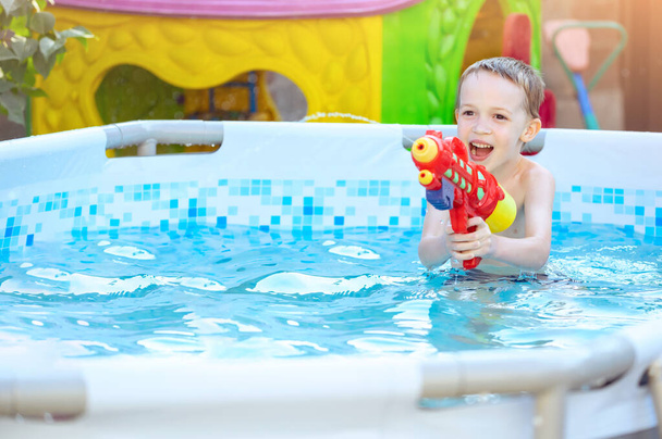 Šťastné smějící se dítě hrající si s vodní pistolí ve venkovním bazénu v letní den. Děti si hrají a učí se plavat. Bazén hračky a vodní zábava pro rodinu s dětmi - Fotografie, Obrázek