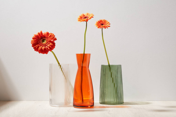 glass vases with gerbera flowers on wooden surface in light room, close view - Photo, Image