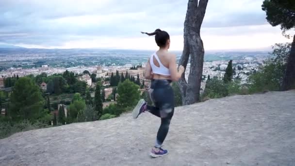 Молодая спортсменка бегает на месте. Медленно движущаяся спортсменка в леггинсах и кроссовках прыгает и поднимает ноги на землю во время тренировки перед Альгамброй в летний день
. - Кадры, видео