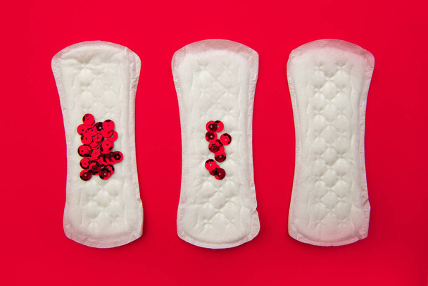 Coussinets menstruels avec des paillettes rouge vif sur fond rouge. Cycle menstruel, fréquence des menstruations. Concept minimaliste de photographie de nature morte - Photo, image