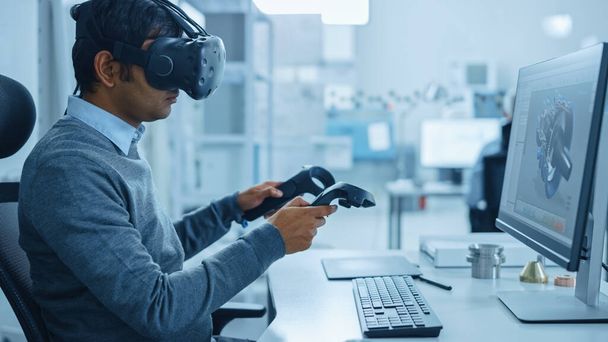 Modern Industrial Factory: Mechanical Engineer Wearing Virtual Reality Headset, Holding Controllers, Uses VR technology for Industrial Design, Development and Prototyping in CAD Software on Computer. - Foto, Imagem