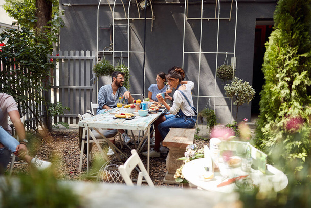 Jongeren genieten van eten, drinken en een heerlijk gesprek in de tuin van het prachtige café - Foto, afbeelding