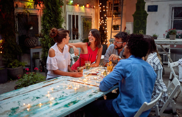 Les jeunes amis profitent d'une conversation amicale au crépuscule au jardin du café - Photo, image