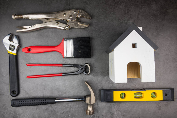 Holzmodell weiße Häuser und Home Repair Handwerkzeuge auf zementgrauem Hintergrund. Konzept Hausreparatur, Heimwerker, Haus renovieren. - Foto, Bild