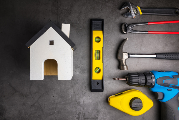Holzmodell weiße Häuser und Home Repair Handwerkzeuge auf zementgrauem Hintergrund. Konzept Hausreparatur, Heimwerker, Haus renovieren. - Foto, Bild