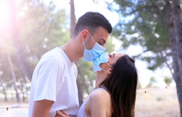 Siyah koruyucu maskelerle öpüşen genç bir çift. Salgın. Coronavirus. Bir adam ve bir kız tıbbi bir maskeyle öpüşüyor. Covid 19. 2020 yazında. Öptüm. - Fotoğraf, Görsel