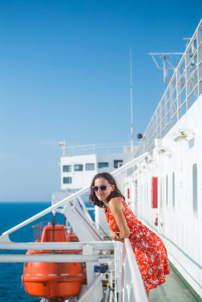 女性がクルーズ船に乗っている、女の子が船のフェンスの近くに立っていると海を見て、フェリーで旅行している、夏のドレスでブルネットは海を賞賛. - 写真・画像