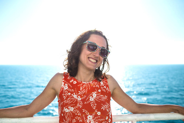Portret van een vrouw op de achtergrond van de oceaan, een vrouw zwemt op een cruiseschip, een meisje staat bij het hek op een schip, reist met de veerboot, een brunette in een zomerjurk bewondert de zee. - Foto, afbeelding
