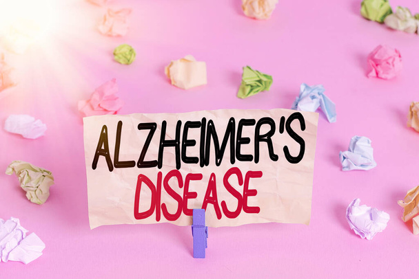 Writing note showing Alzheimers Disease. Business photo showcasing irreversible brain disorder that slowly destroys memory Colored crumpled papers empty reminder pink floor background clothespin. - Photo, Image