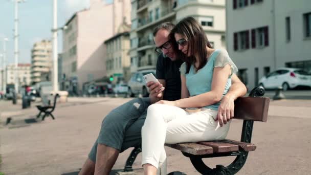 Couple with smartphone sitting on bench - Video, Çekim