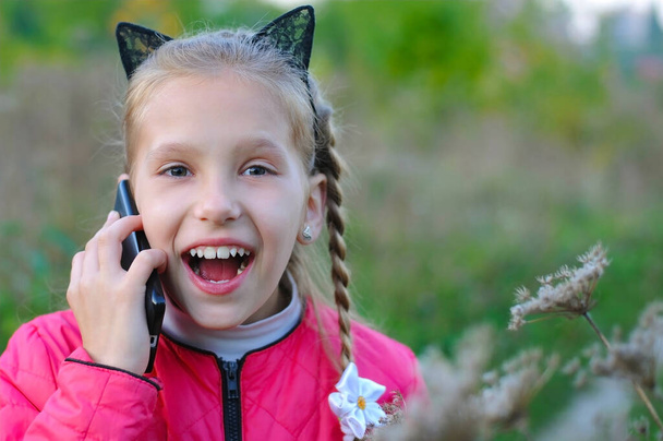 A joyful young girl with surprised face talking on the phone in the park. She is full of positive emotions - Photo, Image