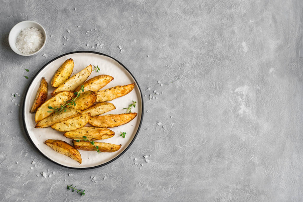 Roasted potato wedges with herbs and sea salt on plate, top view, copy space. Homemade oven baked potato snacks and sour cream sauce. - 写真・画像
