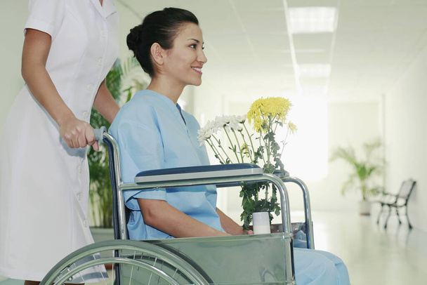Nurse pushing woman on wheelchair, woman holding a vase of flowers - Foto, imagen