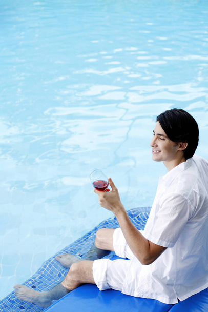Man enjoying a glass of red wine by the pool side - Фото, зображення