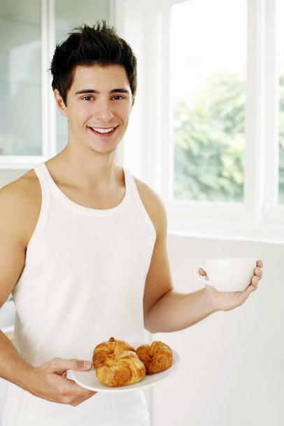 Man holding a plate of croissants and a cup of coffee - Фото, изображение